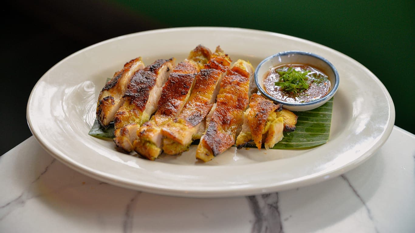 Sliced grilled chicken with dipping sauce on a plate at Homme Thai Supper Club